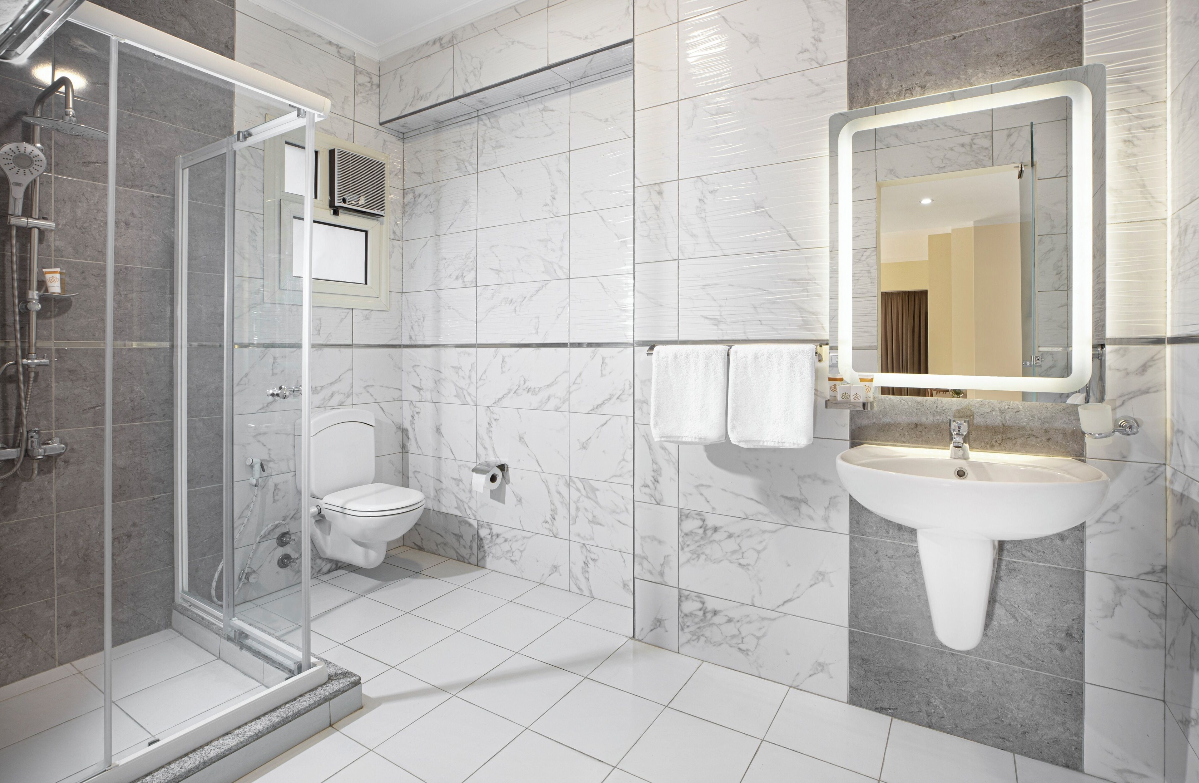 A modern bathroom with a glass shower enclosure, a toilet, a sink with a mirror, and marble tiles.