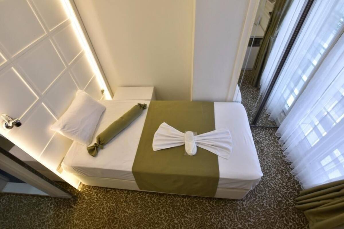 A small, neatly arranged room with a bed, a towel, and a green bedspread.
