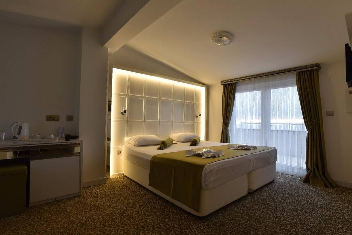 A hotel room with a bed, bedside table, and a large window with curtains.