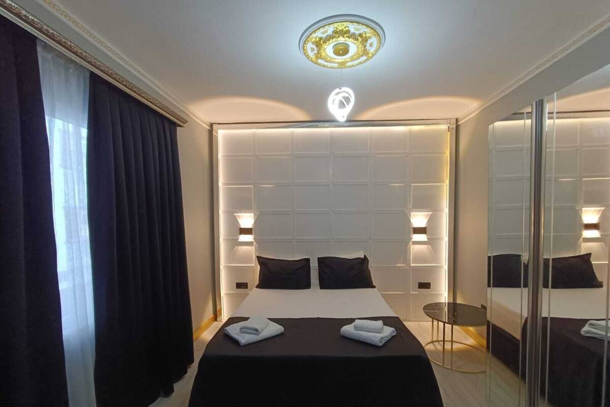 A modern hotel room with a large bed, bedside lamps, a small table, and a mirror.