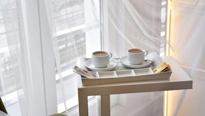 Duas chávenas de café numa bandeja, com jornais, sobre uma pequena mesa perto de uma janela com cortinas leves.
