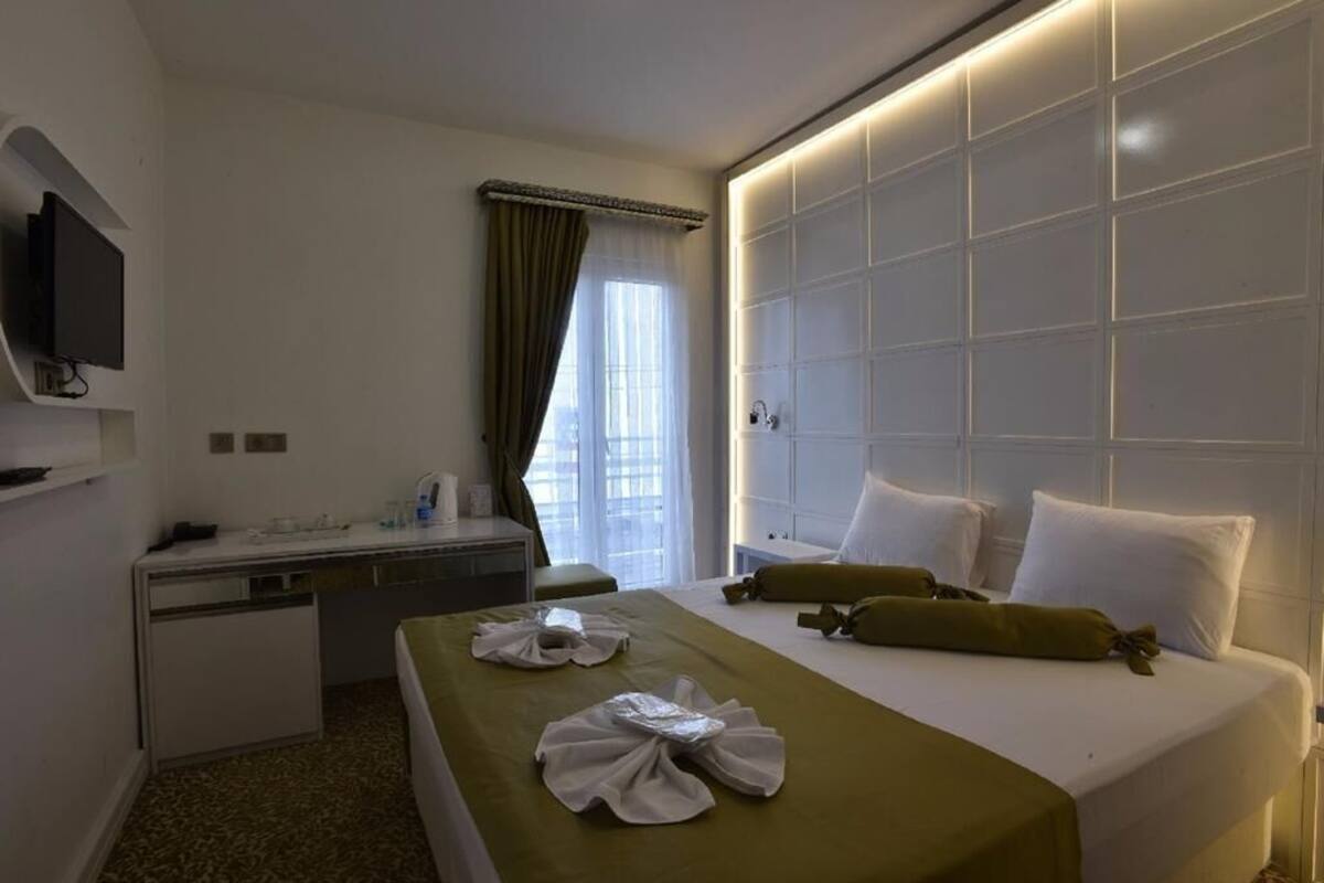 A hotel room with a bed, bedside table, TV, and a window with curtains.
