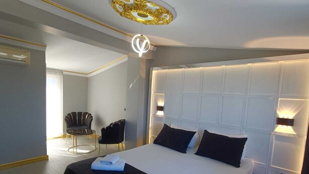 Quarto de hotel com uma cama grande, uma cadeira preta e dourada e uma luminária moderna no teto.
