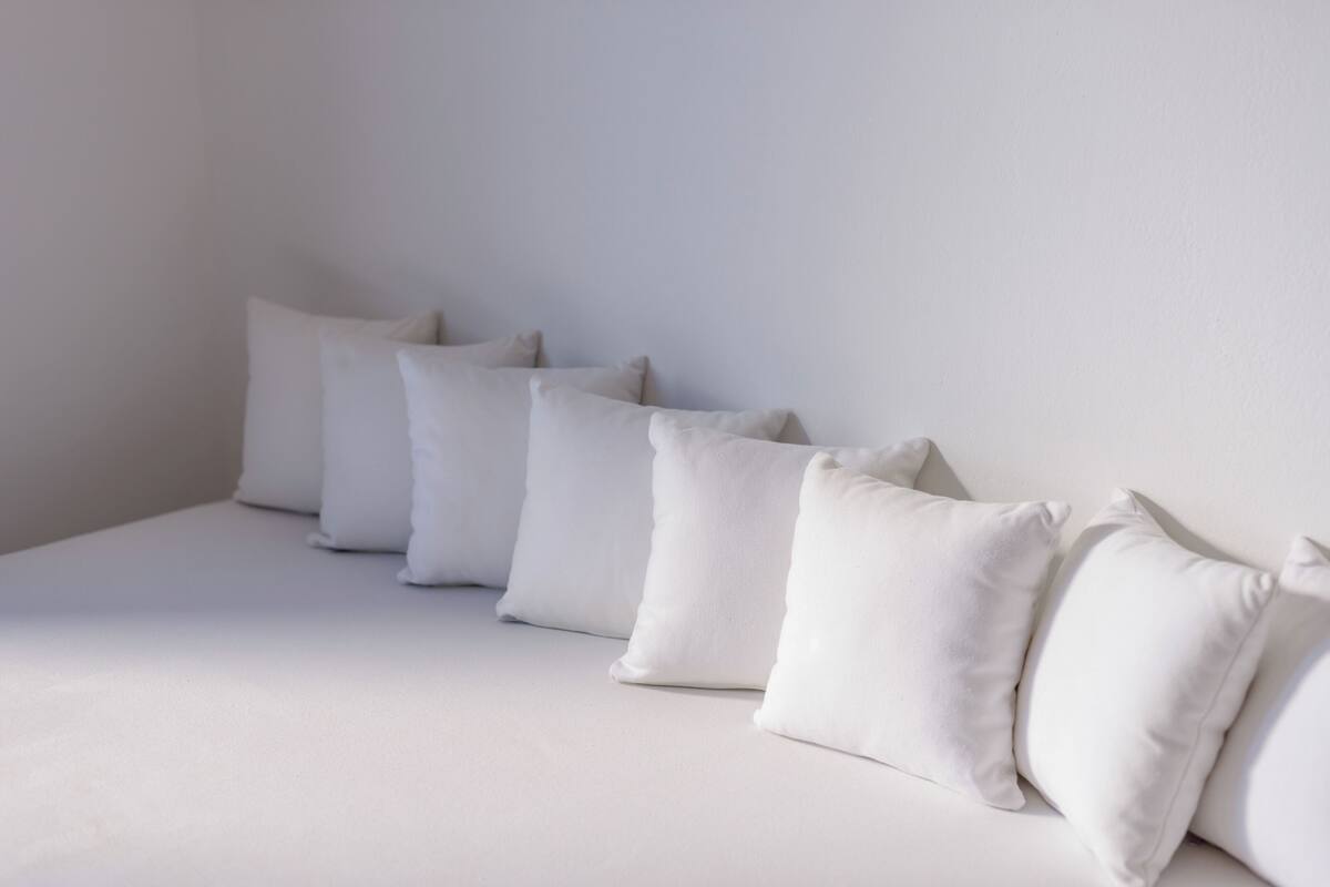 A bed with white bedding and pillows, a plain wall, and a window with natural light.