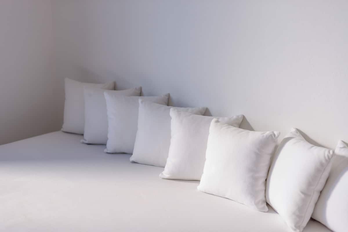 A bed with white bedding and pillows, a plain wall, and a window with natural light.