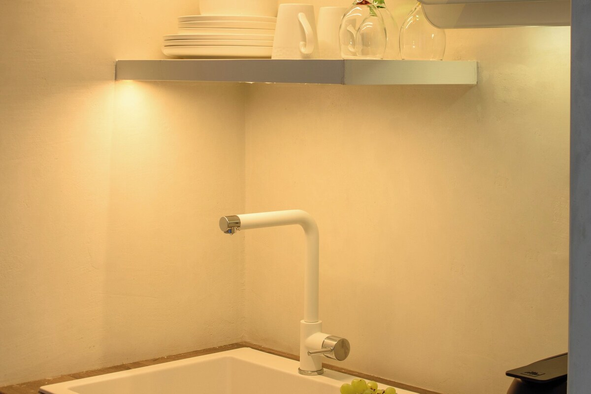 A kitchen with a white sink, a bowl of grapes, and a coffee maker on the counter.