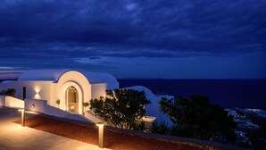 A modern building with a white facade, a curved entrance, and a view of the sea. - LF Suites & Villas (Santorini)