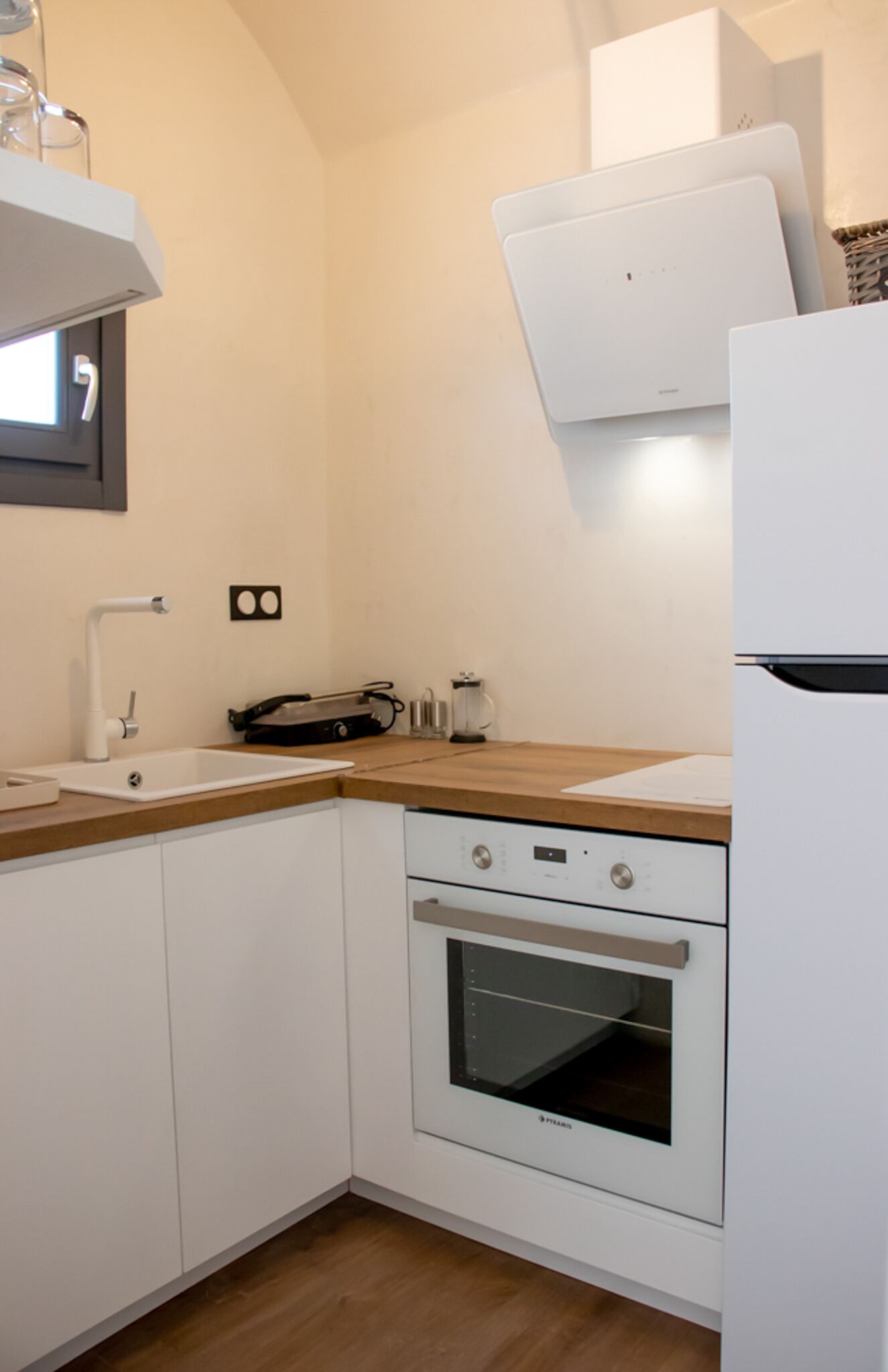 A compact kitchen with white cabinets, a wooden countertop, a built-in oven, and a white refrigerator.