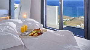 A hotel room with a bed, breakfast tray, and a large window with a view of the sea. - LF Suites & Villas (Santorini)