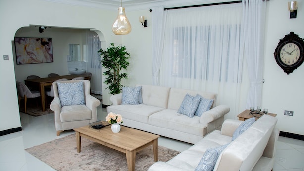 A modern living room with a sofa set, a coffee table, and a dining area with a chandelier. - Stay.Plus Blueberry Villas Eldoret (Eldoret)