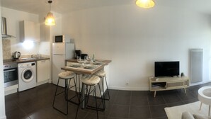 A modern apartment with a kitchen, dining area, and living room. It includes a washing machine, a dining table with bar stools, a TV, and a sofa. - VANNES CENTER QUIET-COZY-T2 WITH PRIVATE PARKING-TERRACE-WIFI (Vannes)
