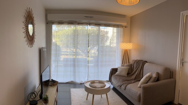 A modern living room with a sofa, a TV, a lamp, and a large window with curtains. - VANNES CENTER QUIET-COZY-T2 WITH PRIVATE PARKING-TERRACE-WIFI (Vannes)