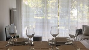 A dining table set for four with wine glasses and plates, positioned near a window with a view of trees. - VANNES CENTER QUIET-COZY-T2 WITH PRIVATE PARKING-TERRACE-WIFI (Vannes)