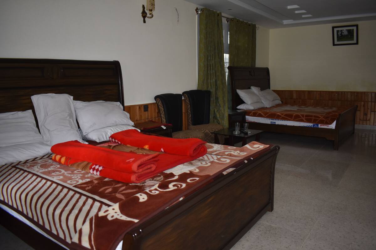 Habitación de hotel con dos camas, cabecero de madera, una mesita y cortina verde.