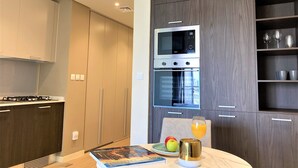 Et moderne køkken med indbyggede apparater, et spiseområde med et bord dækket til morgenmad og udsigt over byen gennem vinduet.