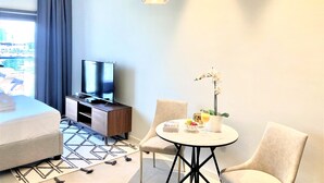 Une chambre d’hôtel moderne équipée d’un lit, d’une télévision, d’une table à manger avec des chaises et offrant une vue sur la ville par la fenêtre.