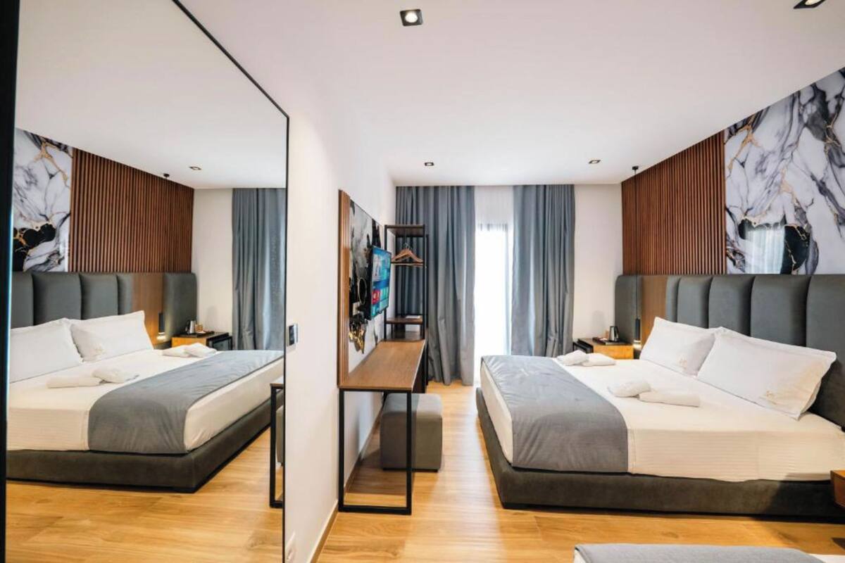 A modern hotel room with two beds, a wooden floor, a large mirror, and artwork on the walls.
