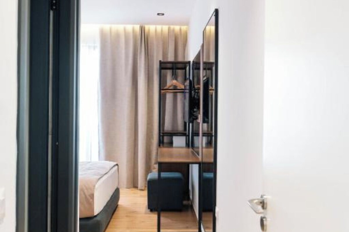 A narrow hallway leading to a bedroom with a bed, a desk, and a wardrobe.
