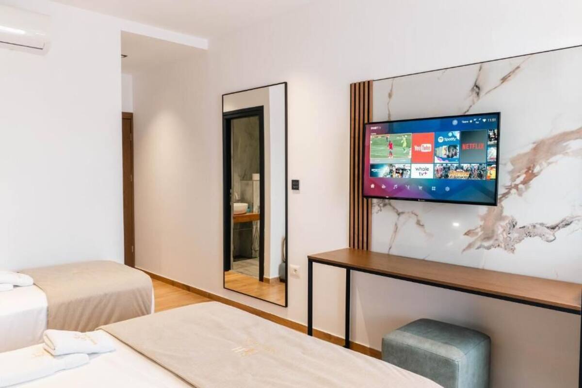 A hotel room with two beds, a TV mounted on the wall, a mirror, and a wooden console table.