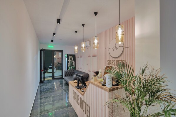 A hotel reception area with a modern design, including a reception desk, a sofa, and hanging pendant lights.