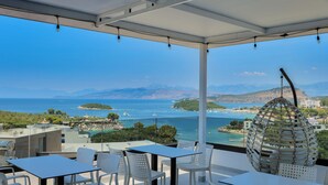 A terrace with a table and chairs, overlooking a coastal view with mountains and the sea. - Siars Hotel (Ksamil)