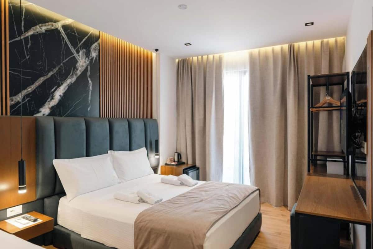 Una habitación de hotel moderna con una cama grande, una mesita de noche de madera, un escritorio y un armario.