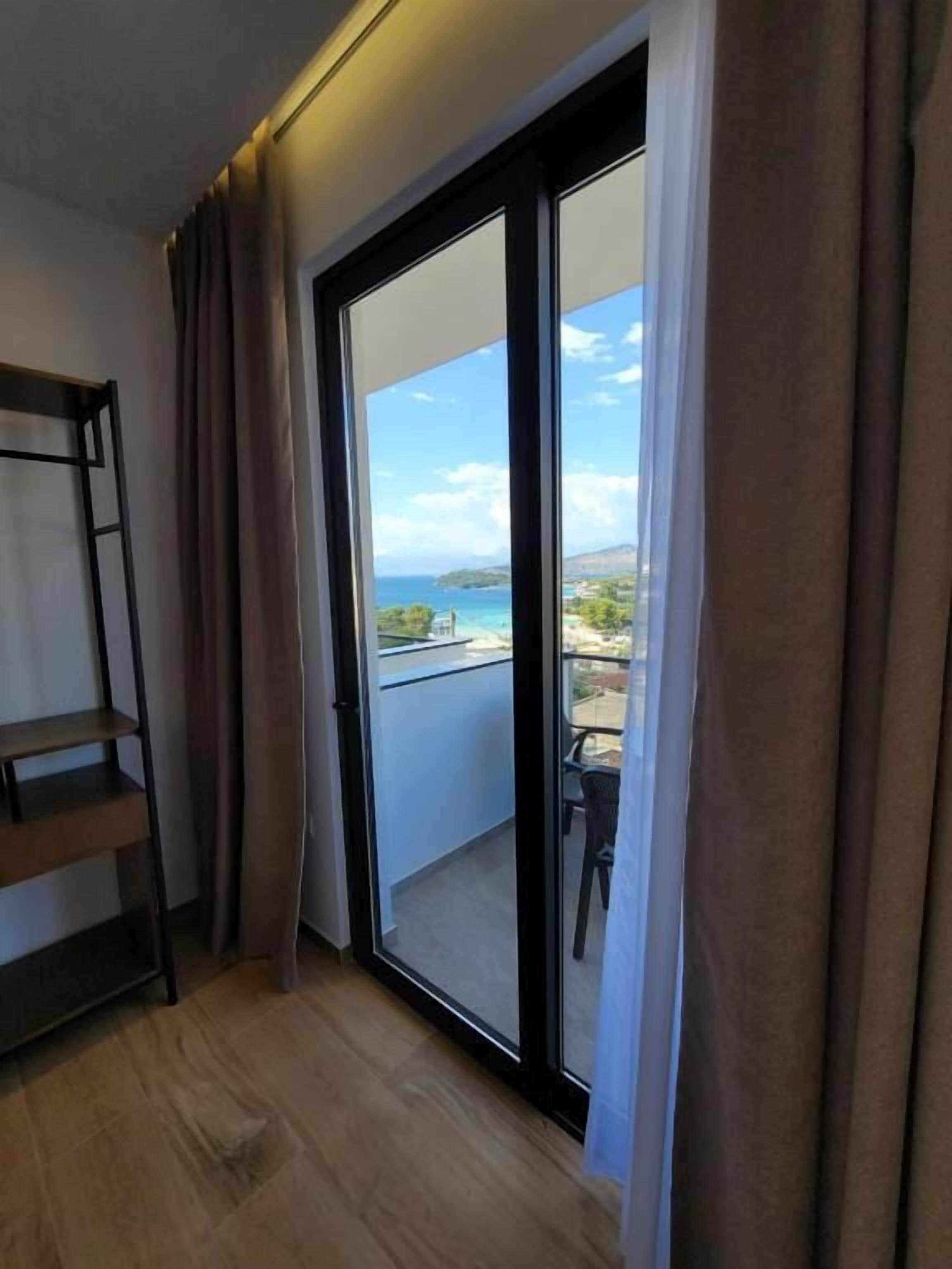 Une pièce dotée d’une porte-fenêtre coulissante donnant sur un balcon avec vue sur la mer et une île au loin.