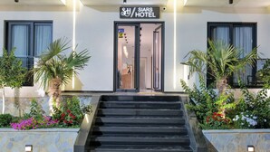 A hotel entrance with a sign reading "SIARS HOTEL," a set of stairs leading up to the entrance, and a garden with various plants and flowers. - Siars Hotel (Ksamil)