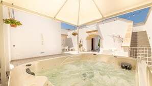 Area con vasca idromassaggio, rivestimento bianco, zona salotto coperta e una scala che conduce a un livello superiore.