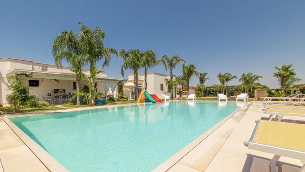 Una piscina con uno scivolo, circondata da palme e lettini.