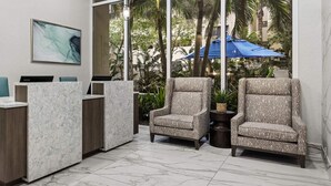 Un área de recepción con piso de mármol, un mostrador de recepción, dos sillones y obras de arte en las paredes.