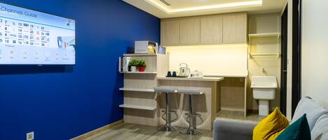 A modern hotel room with a blue accent wall, a kitchenette, a bar area, and a seating area with a sofa and a coffee table.
