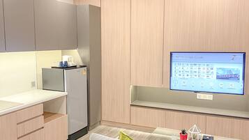 A modern kitchen with a built-in refrigerator, a flat-screen TV mounted on the wall, and a grey sofa in the living area.