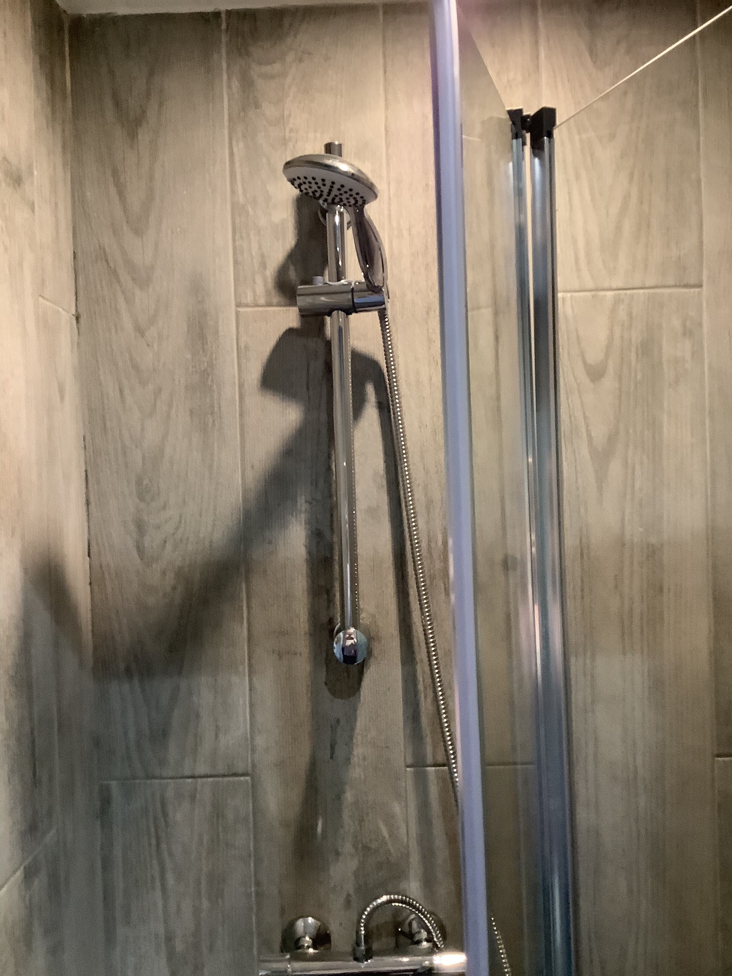 A shower with a handheld showerhead and a vertical rain showerhead, mounted on a wooden wall.