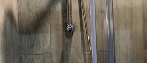 A shower with a handheld showerhead and a vertical rain showerhead, mounted on a wooden wall.