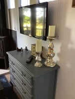 A grey dresser with multiple drawers, a remote control, and two candlesticks with candles.