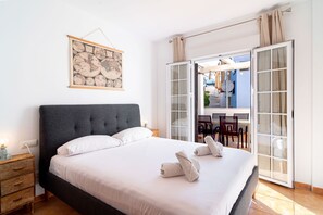 A bedroom with a large bed, a nightstand, a wall-mounted globe, and a sliding glass door leading to a dining area. - Azahara En Suite by Casasol (Nerja)