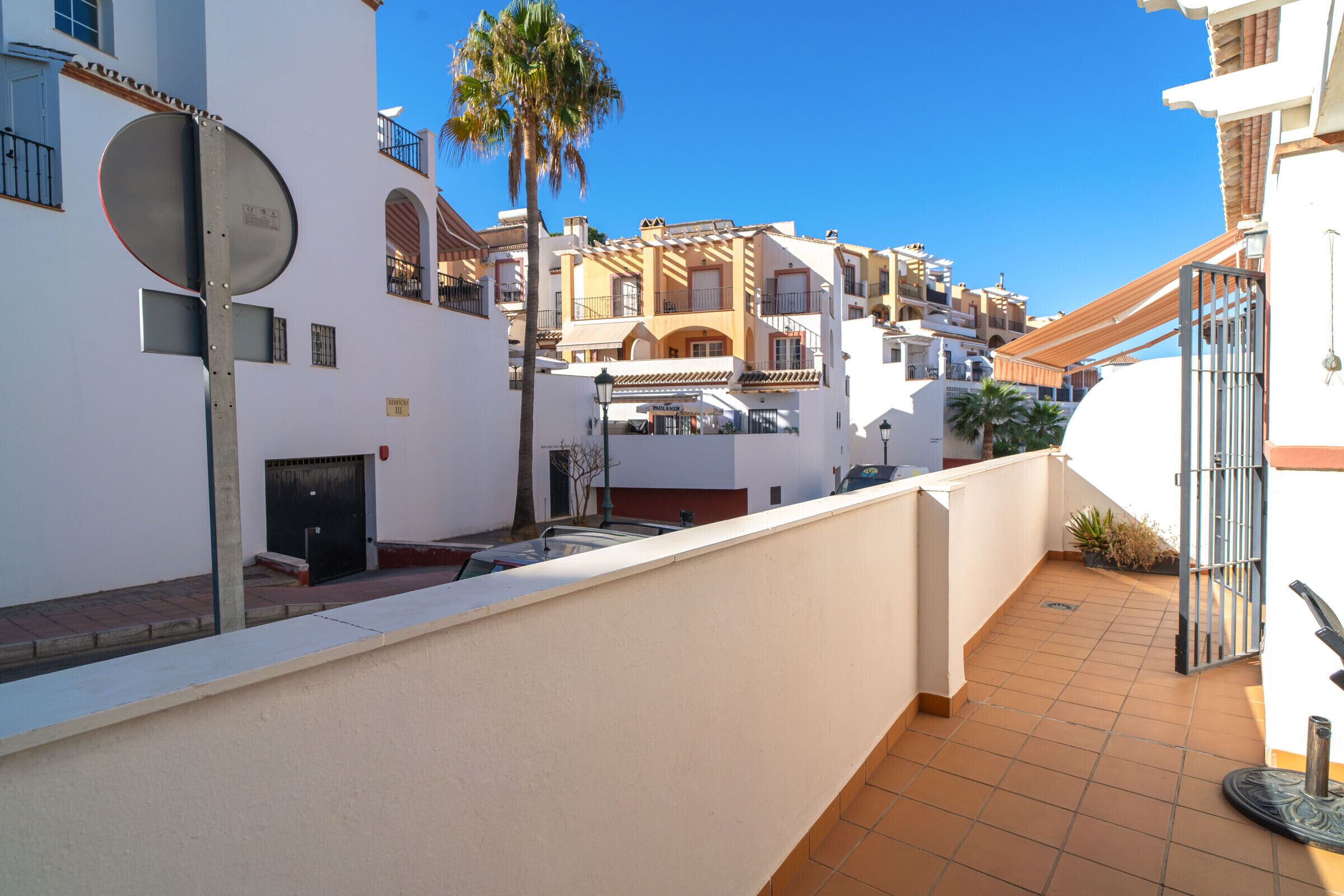 Zona residencial con edificios blancos, una palmera y un balcón con tejas.
