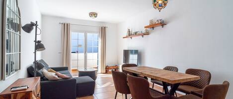 Una sala de estar moderna con un sofá, una mesa de comedor con sillas y una cocina con estantes.