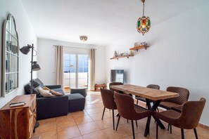 A modern living room with a sofa, a dining table with chairs, and a kitchen area with shelves. - Azahara En Suite by Casasol (Nerja)