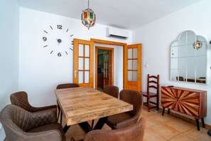 A dining area with a wooden table and chairs, a wall clock, an air conditioning unit, and a mirror. - Azahara En Suite by Casasol (Nerja)