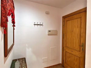 A hallway with a wooden door, a wall-mounted air conditioning unit, a wall-mounted light switch, and a coat rack with hooks.