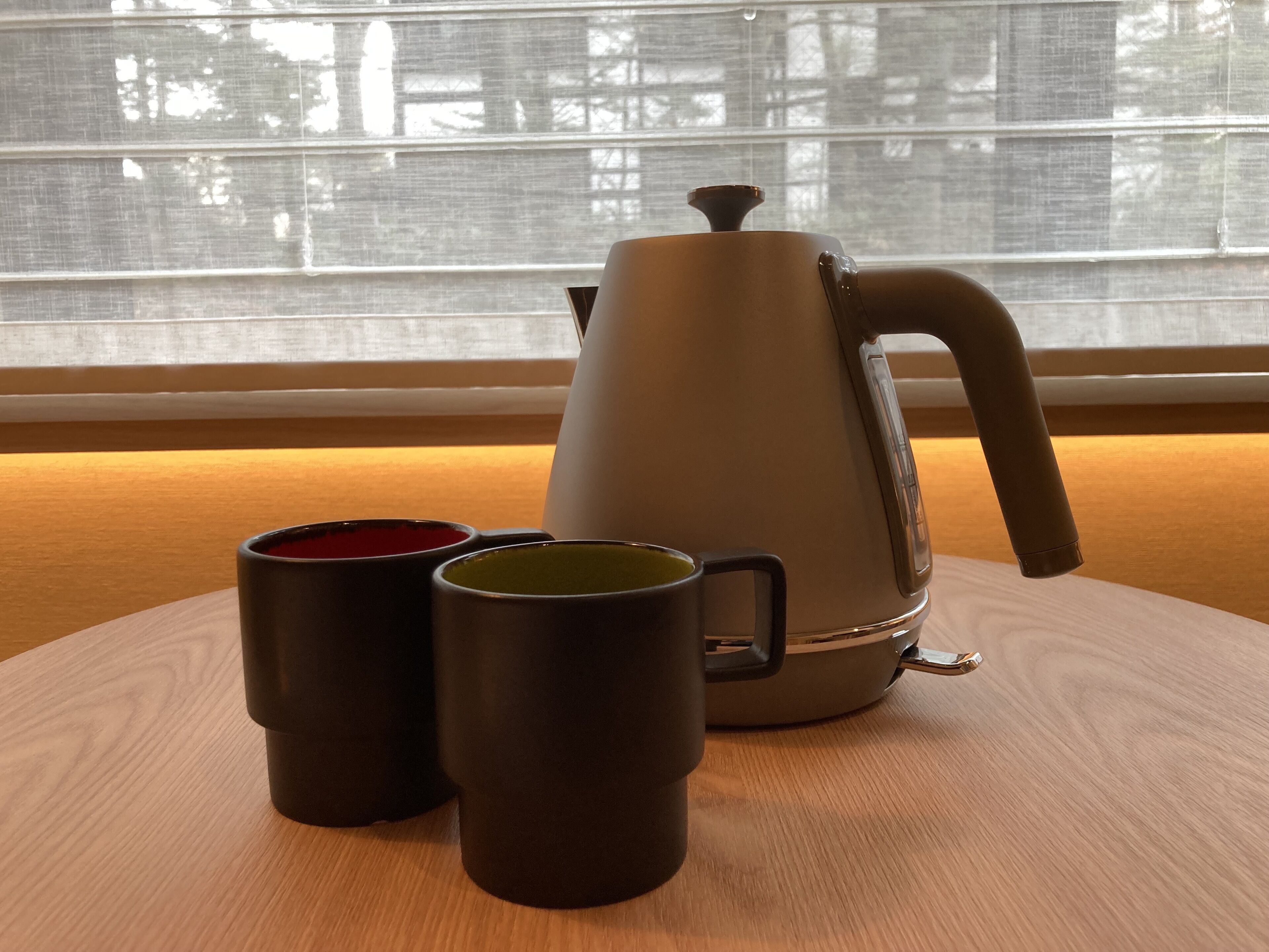 A coffee maker on a wooden table with two mugs.