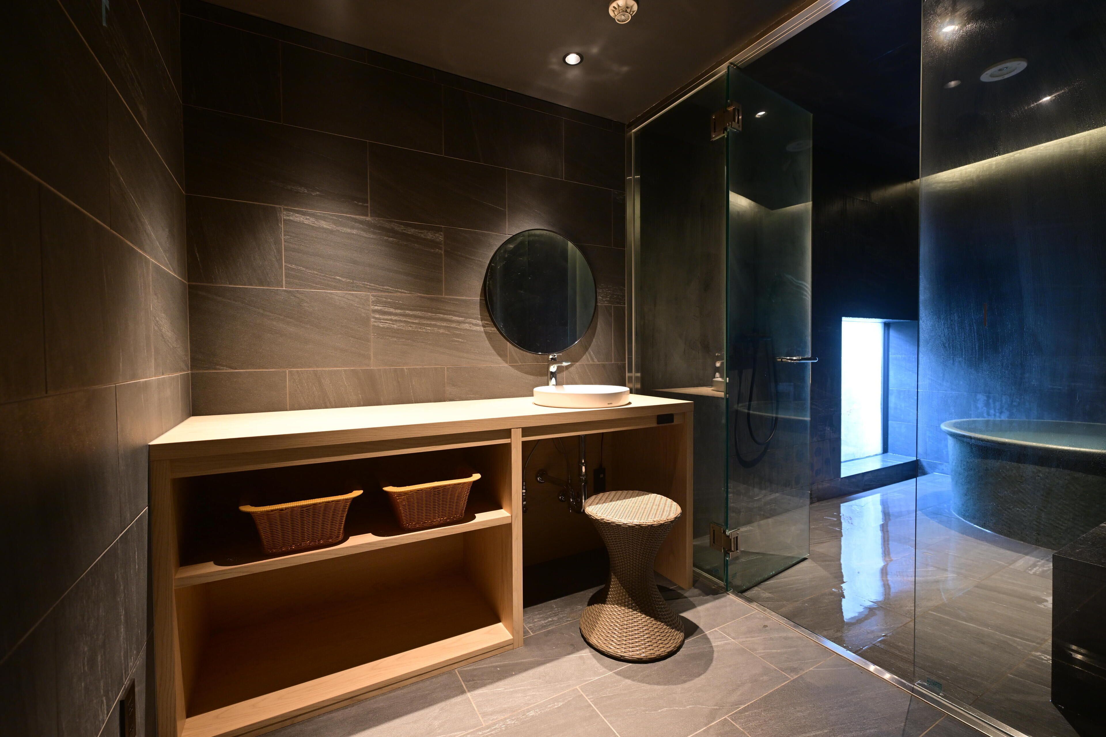 A modern bathroom with a wooden vanity, a round mirror, and a glass shower enclosure.