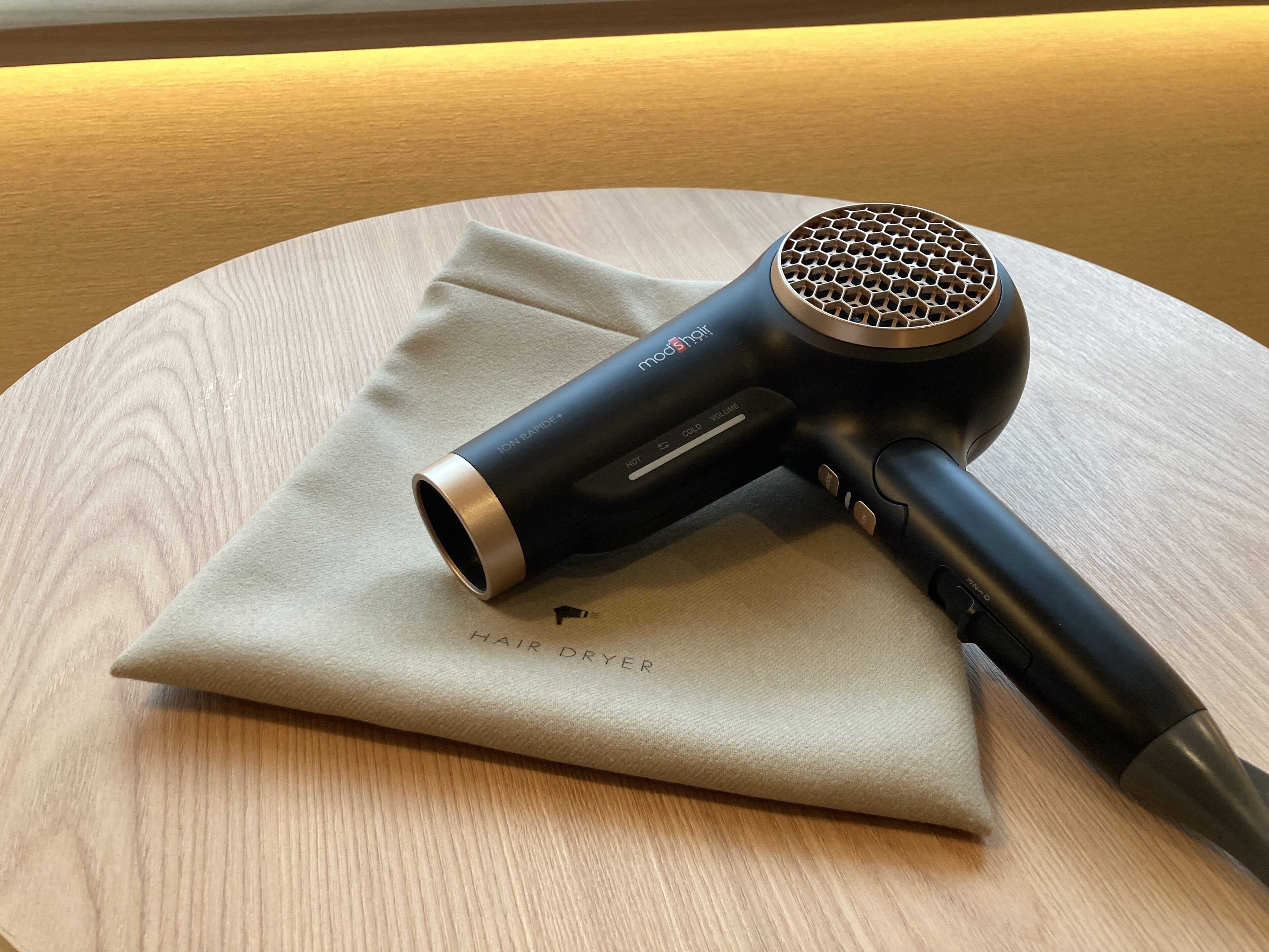 A hair dryer on a round wooden table with a beige cloth.