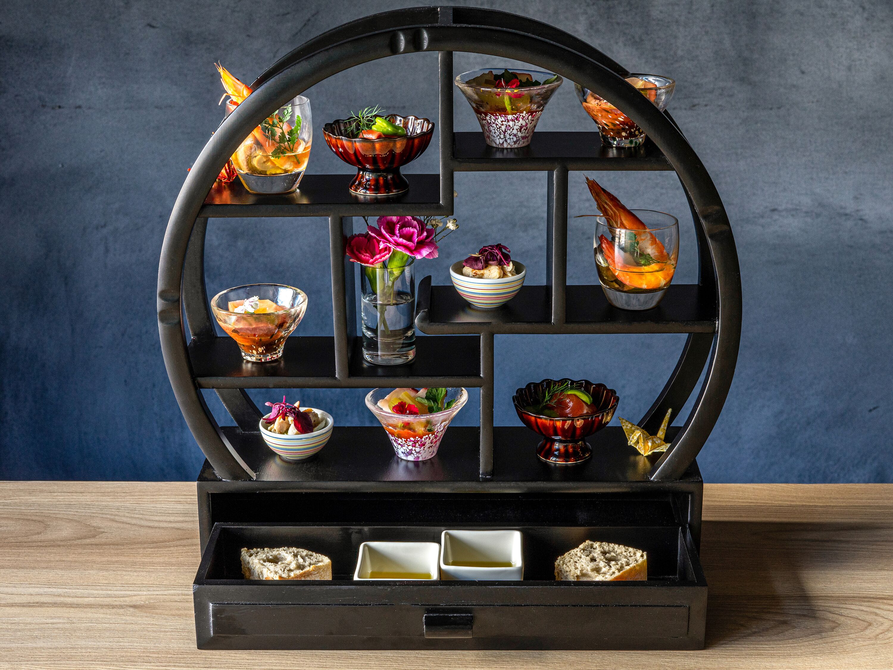 A black, circular display stand with multiple compartments holding various food items and drinks.