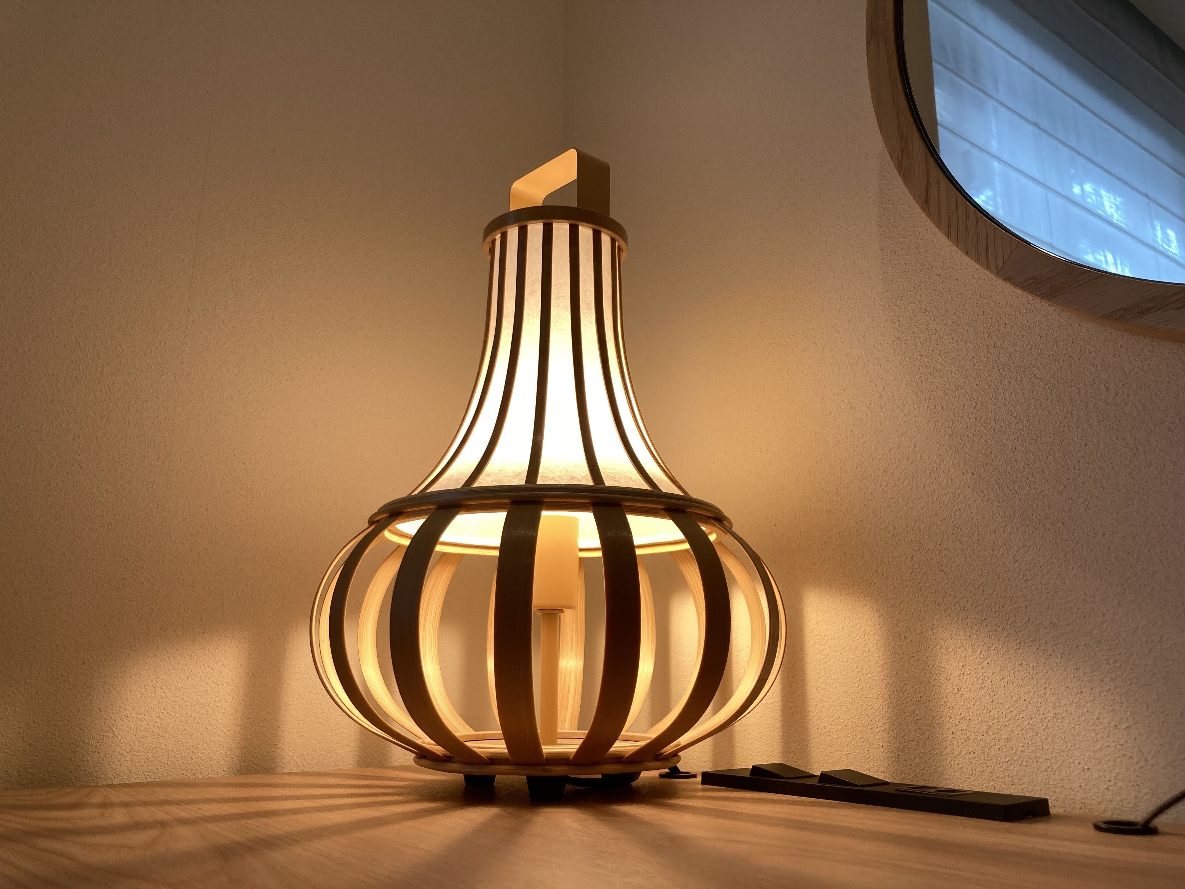 A modern lamp with a cylindrical base and vertical slats, placed on a wooden surface.