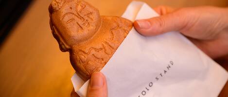 A hand holding a baked item with a face imprint, placed on a white paper labeled "TOLO STAND".