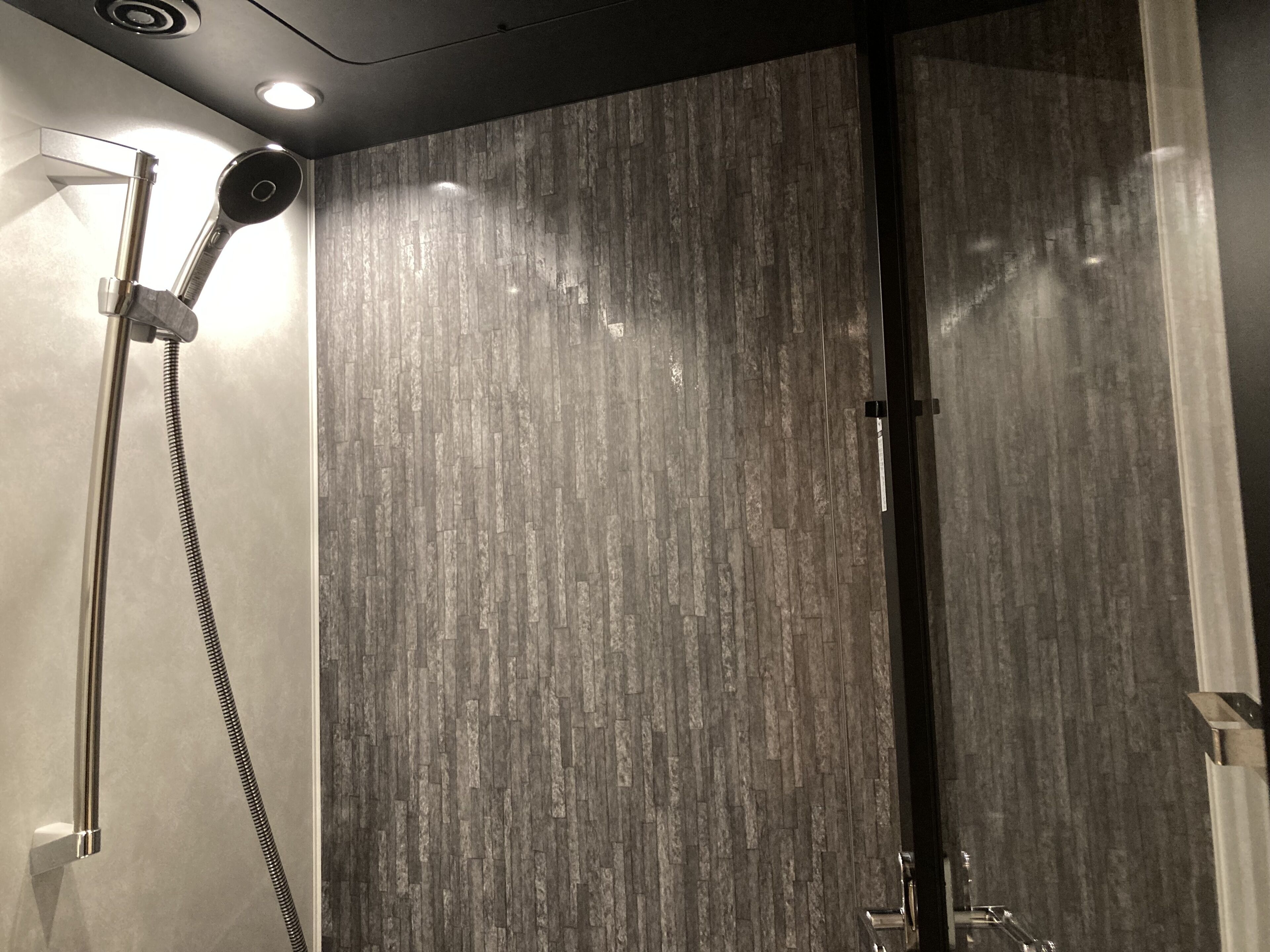 A modern shower with a wooden-texture wall, a handheld showerhead, and a wall-mounted faucet.