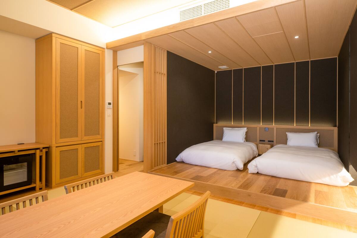 Ein Hotelzimmer mit Holzboden, zwei Betten mit weißer Bettwäsche, einem Holztisch und einem fest installierten Fernseher.
